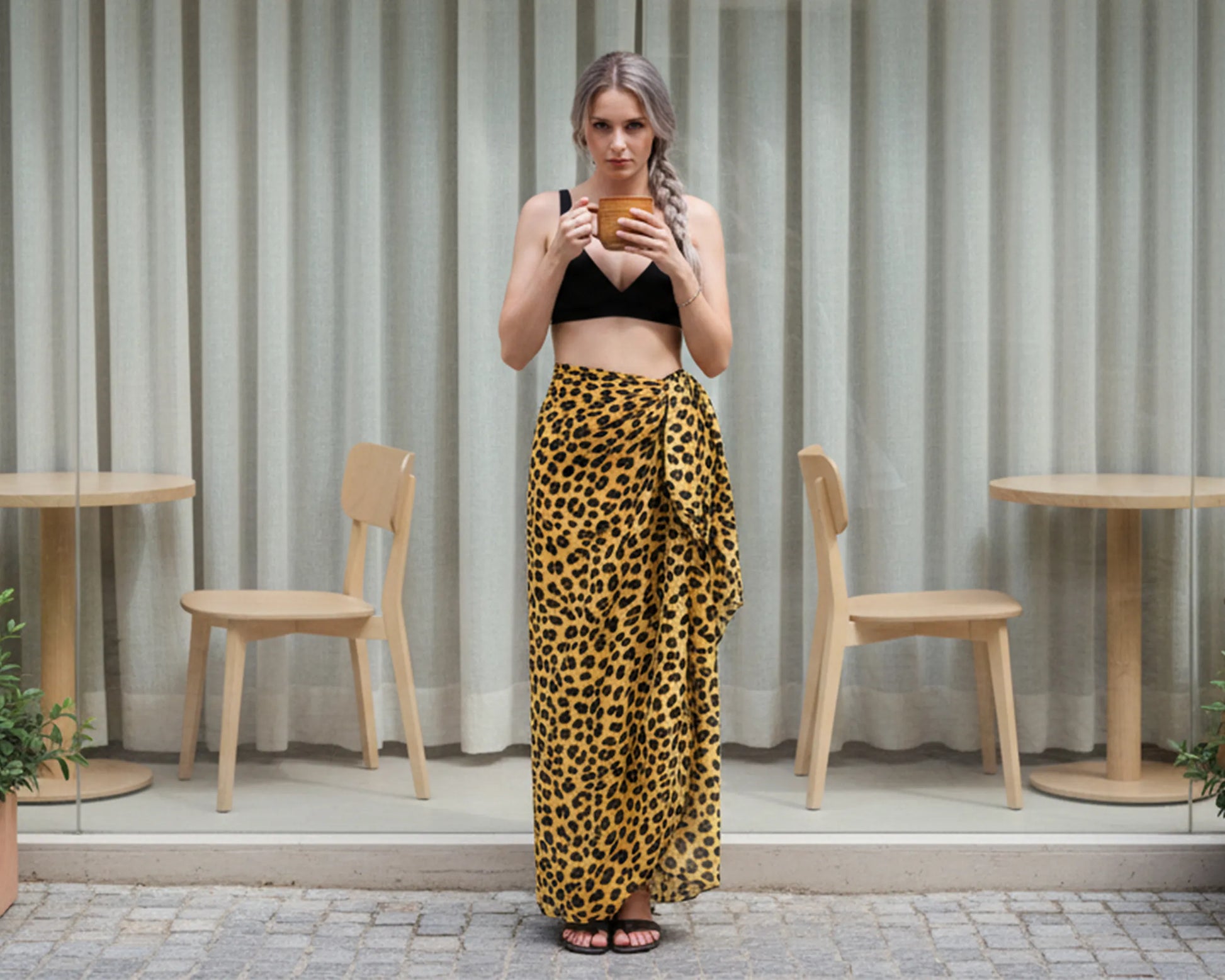 Woman in leopard print sarong and black top standing in front of a cafe window.