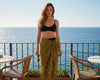 Woman in black top and leopard print skirt standing on a balcony with ocean view